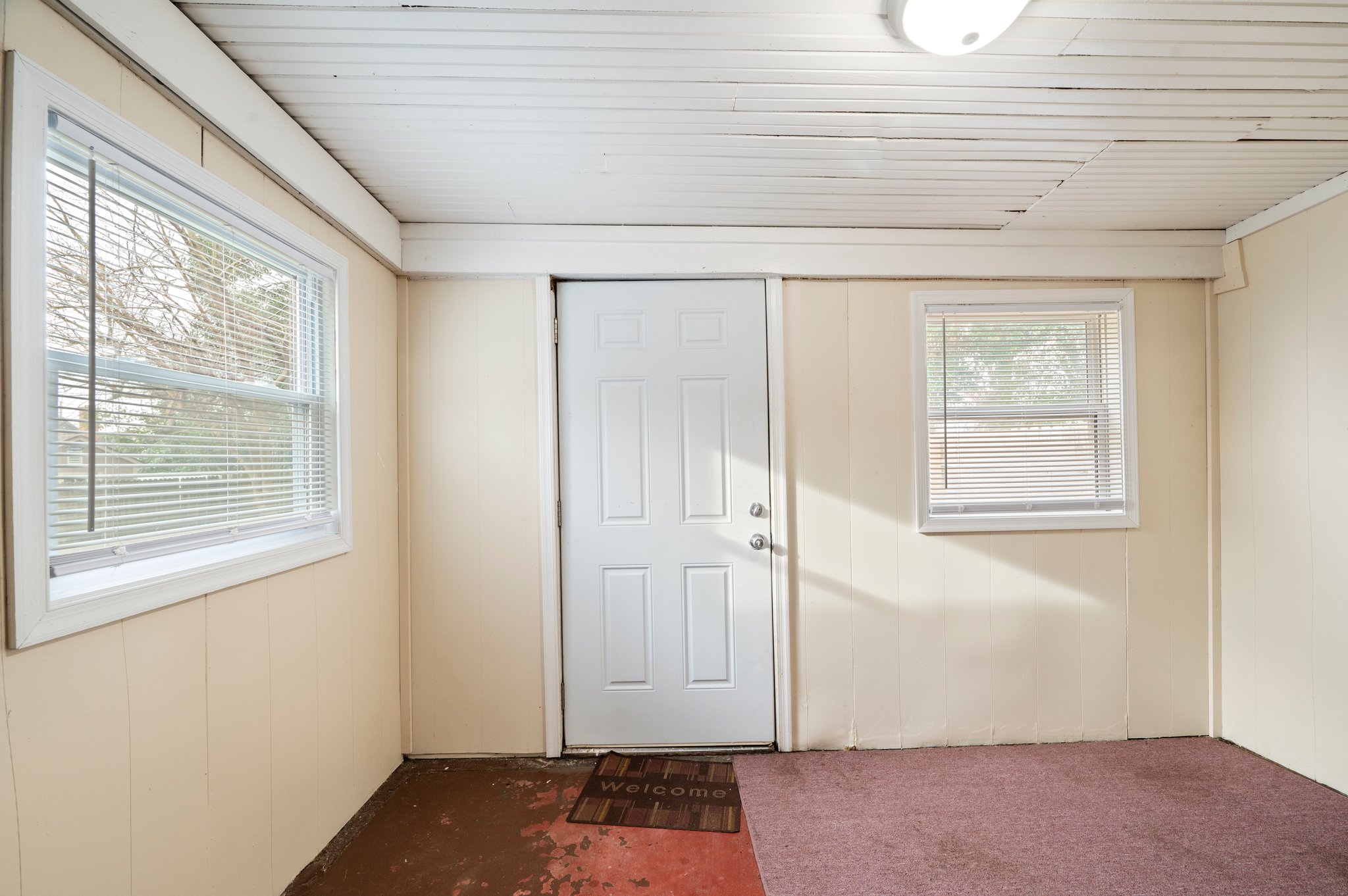 Enclosed porch with white door, beige walls, and two windows.