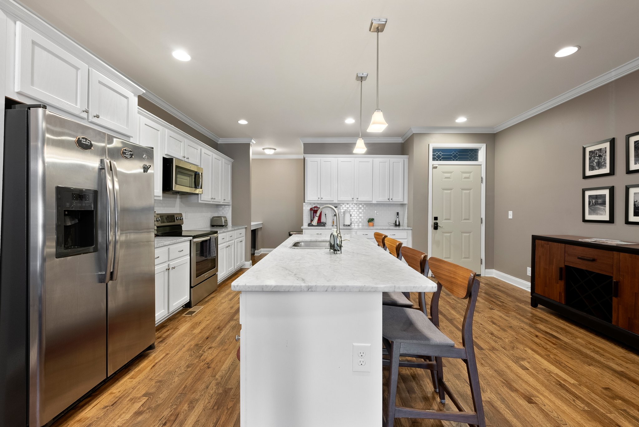 Kitchen view from dining area showing bar seating and elegant pendant lights