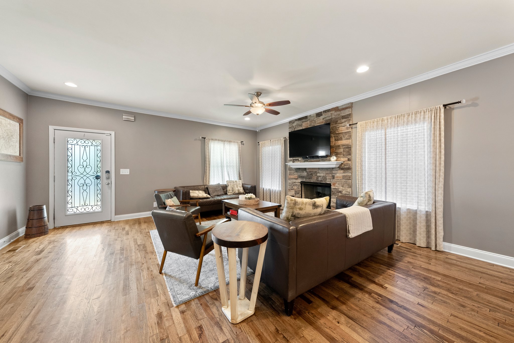 Living room with leather sofas, stone fireplace, and wall-mounted TV