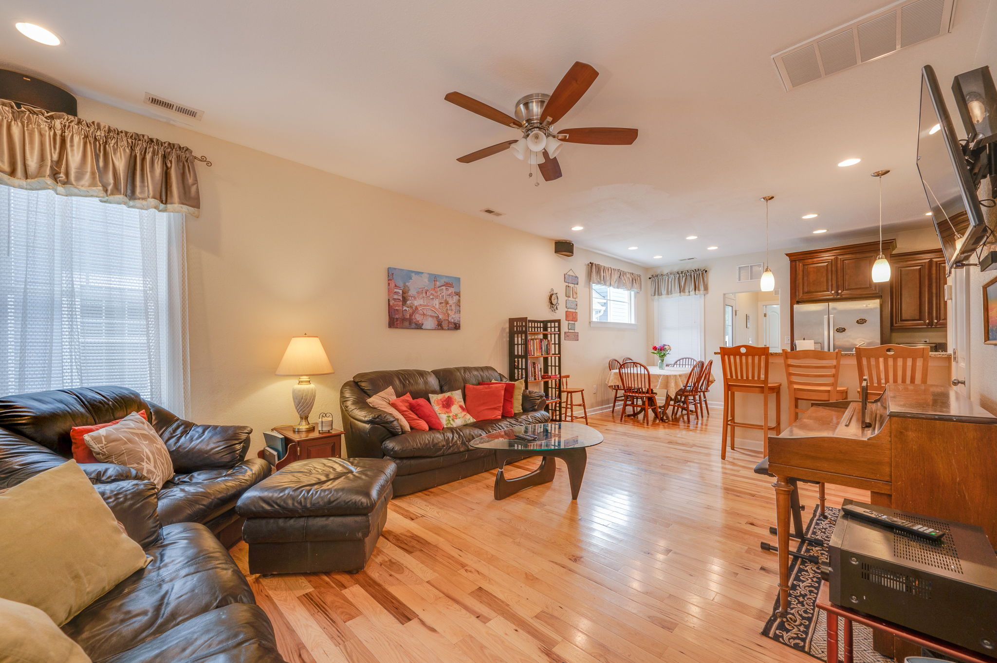 Spacious living room with leather sofas, hardwood floors, and a ceiling fan.