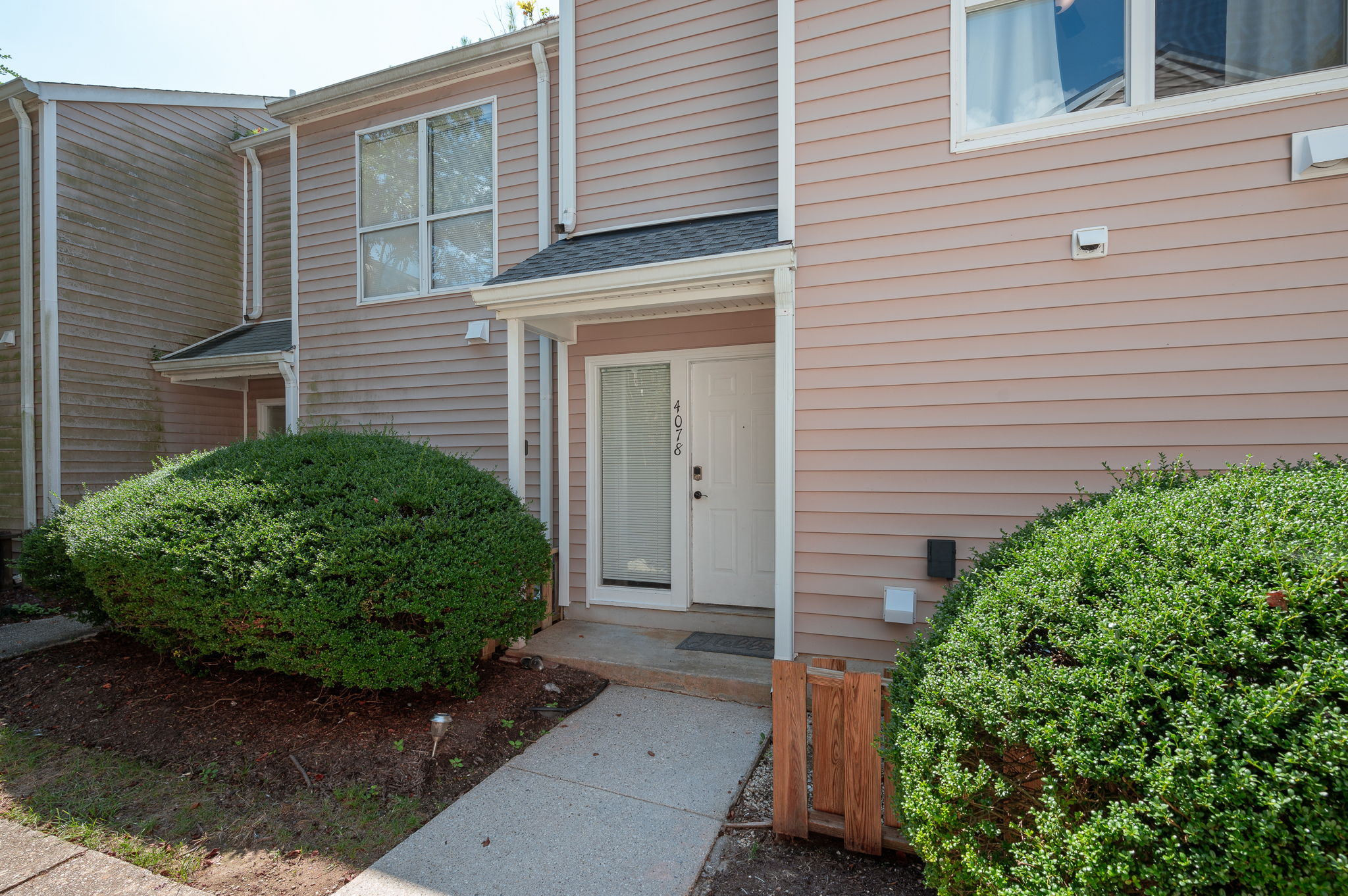 Townhouse front entrance with white door and neatly trimmed hedges