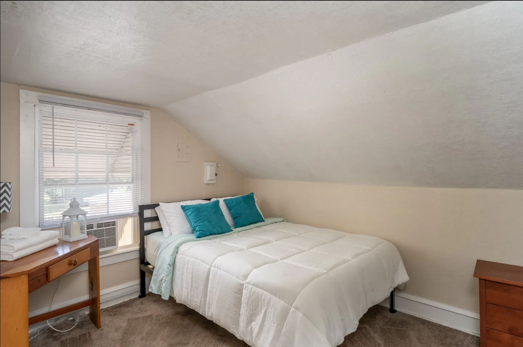 Cozy bedroom with white bedding, blue pillows, and a small desk.