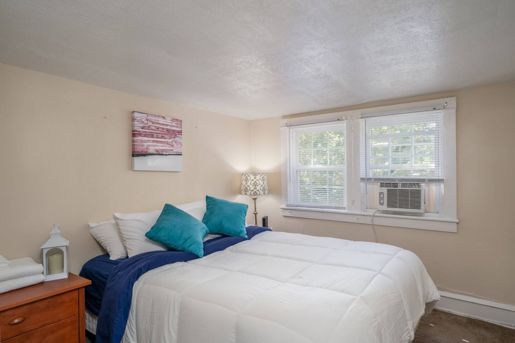 Bright bedroom with two windows, a white bed, and a nightstand.