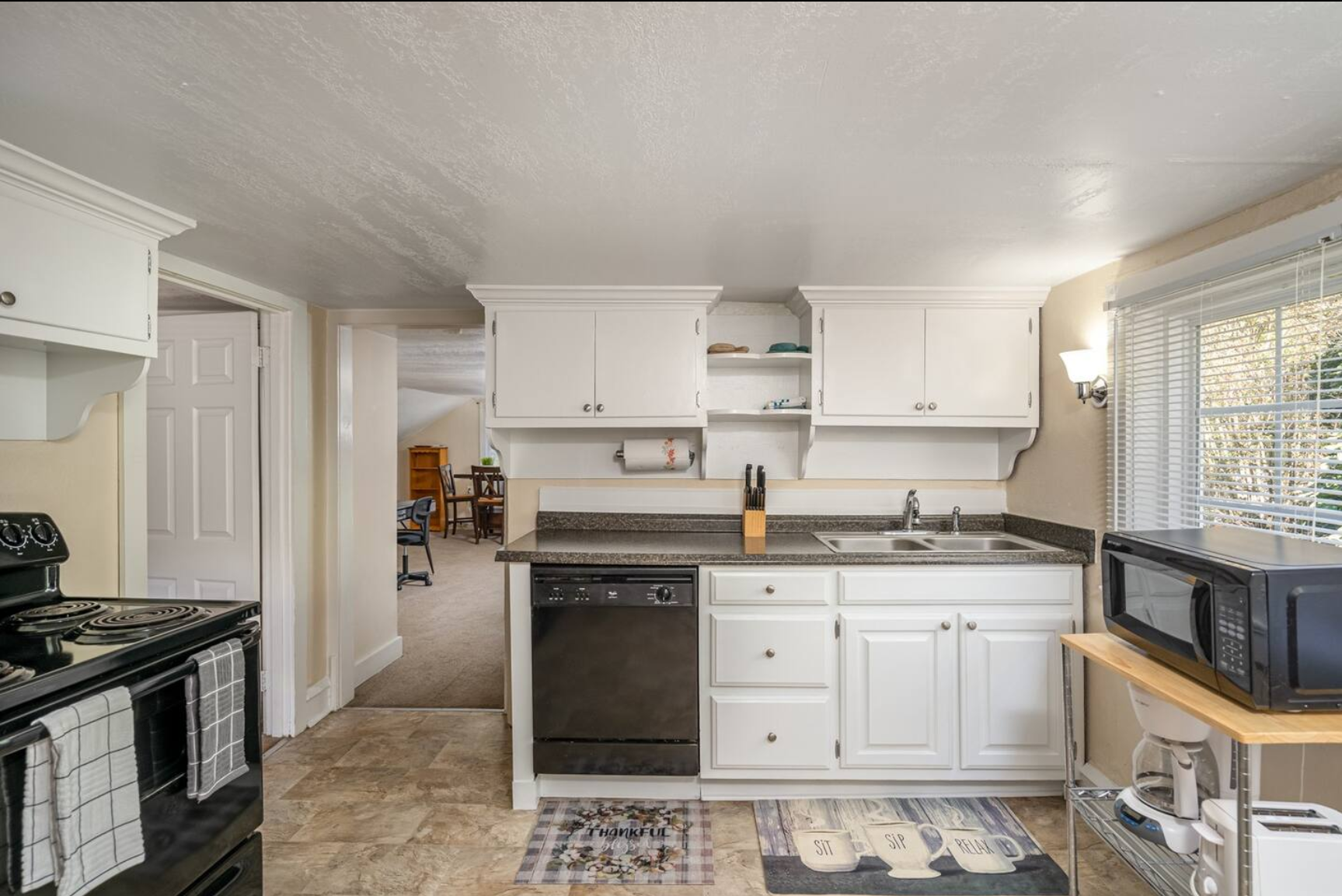 Spacious kitchen with white cabinets, black appliances, and open shelving.
