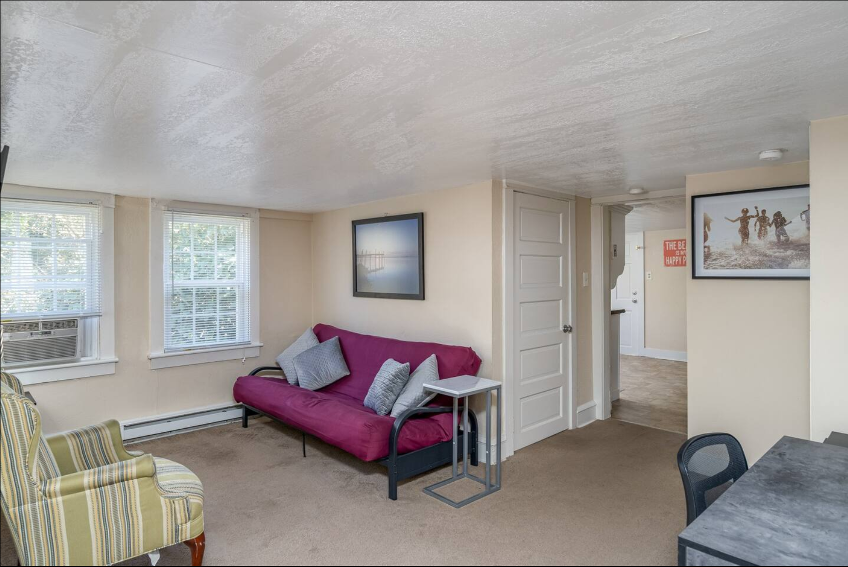 Living room with a purple futon, striped armchair, and framed artwork.