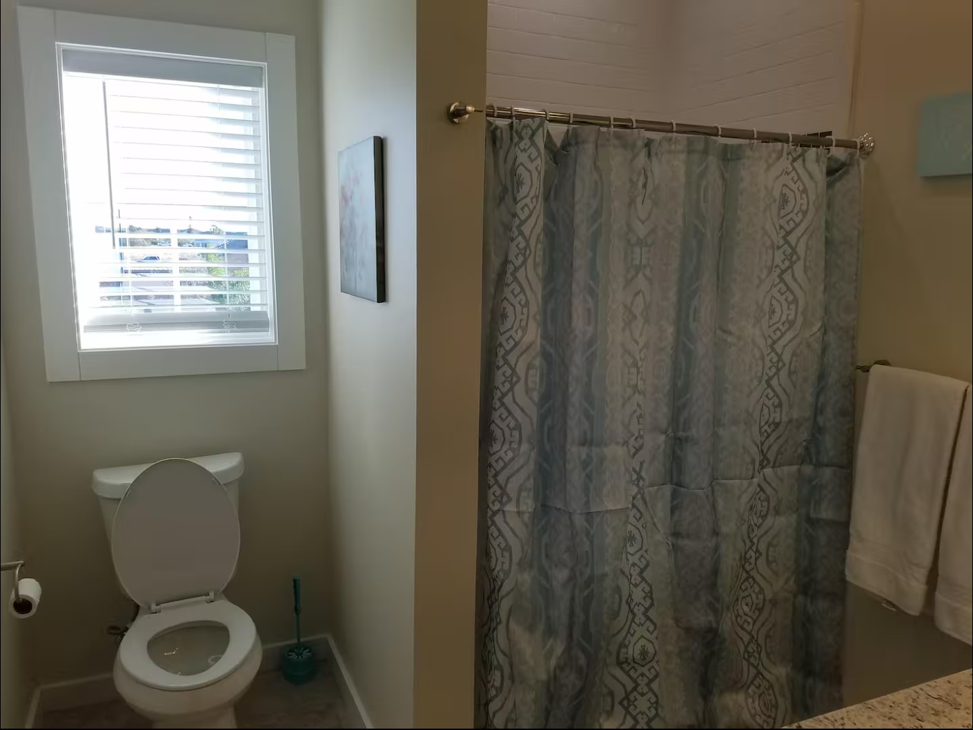 Toilet area next to shower with blue patterned curtain and window