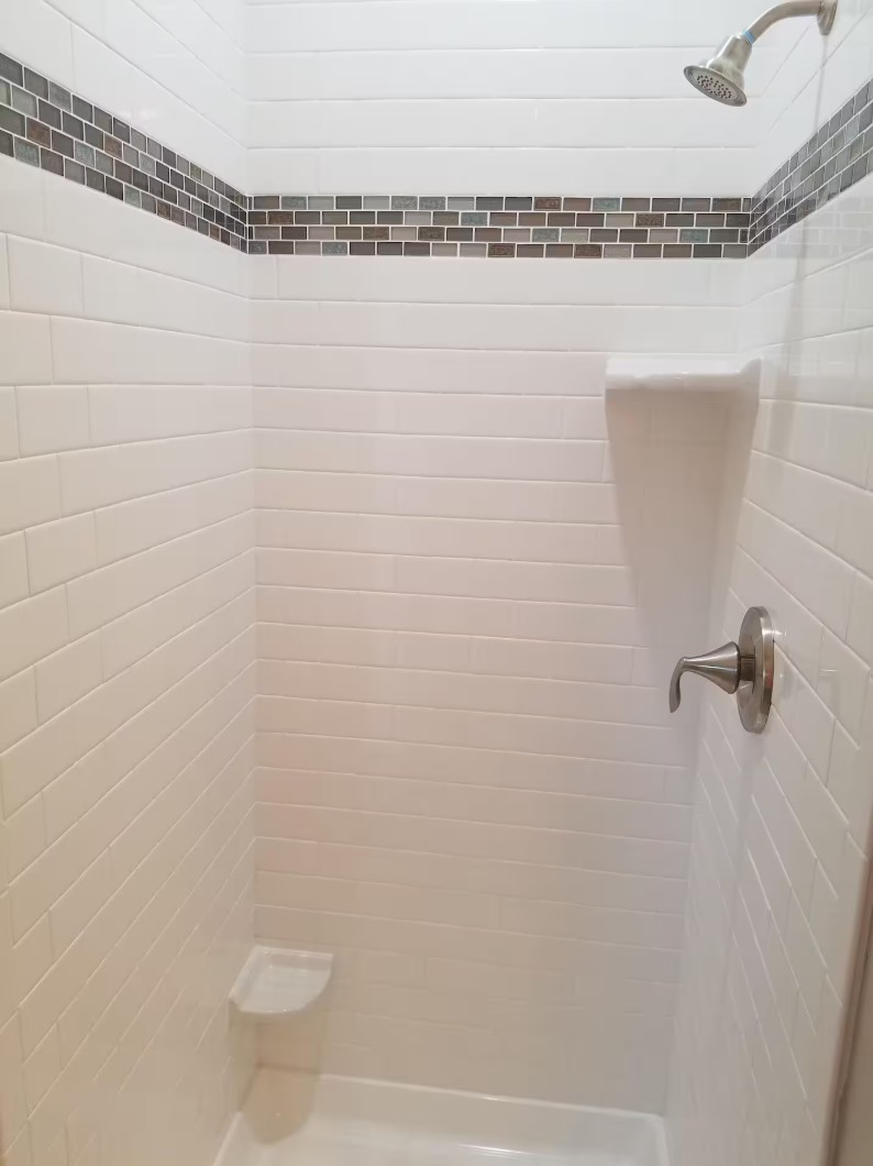 Clean white tiled shower with modern fixtures and shelf