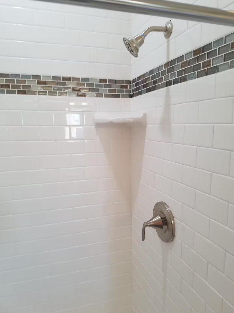White tiled shower with accent strip and metal fixtures