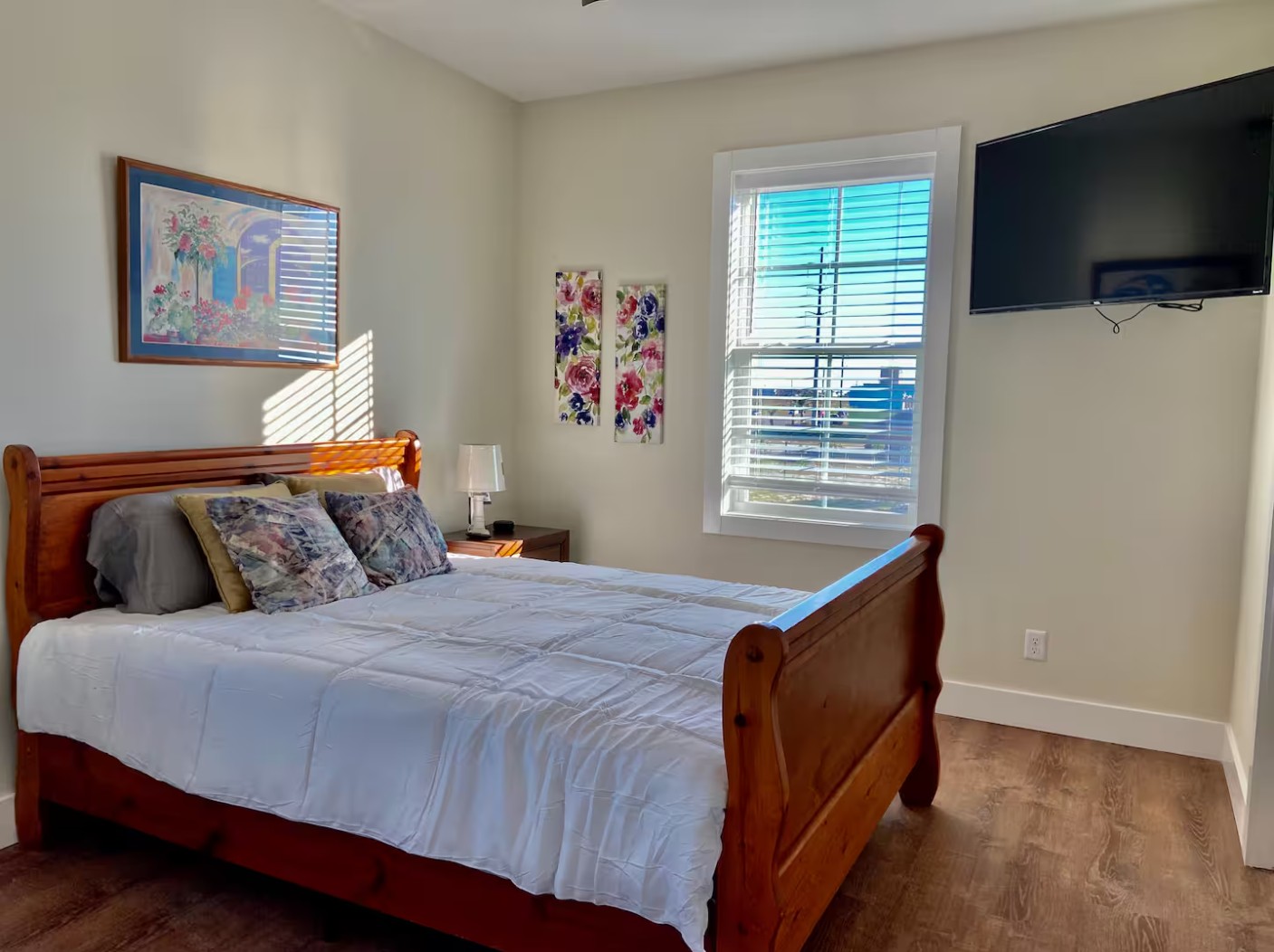Bright bedroom with wooden sleigh bed, wall art, and mounted TV